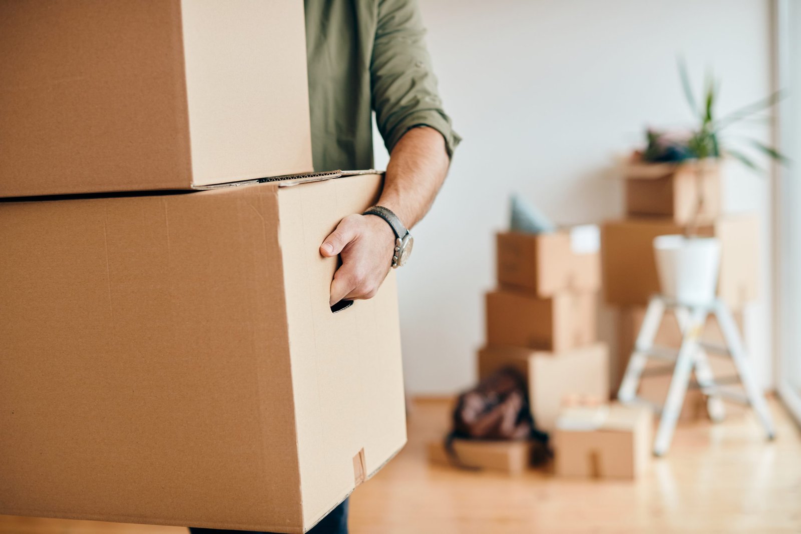 closeup man carrying cardboard boxes while relocating into new apartment scaled