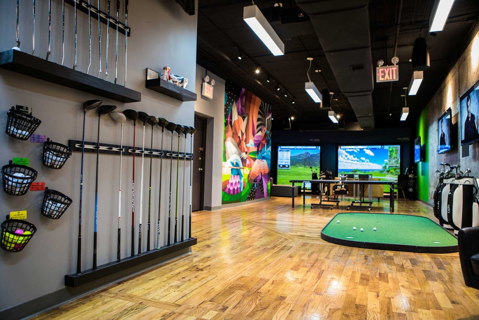 Interior of Five Iron Golf Clayton featuring golf simulators, putting green, and club displays.