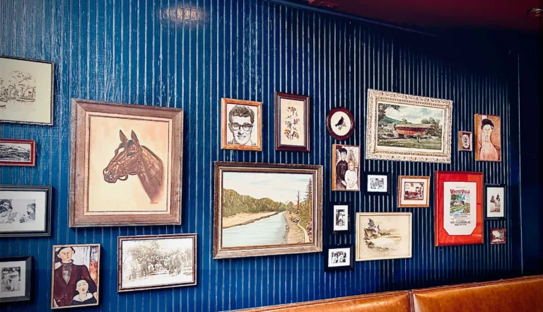 Eclectic gallery wall at Nettie’s Pizza St. Louis featuring vintage artwork and framed illustrations on navy paneling.