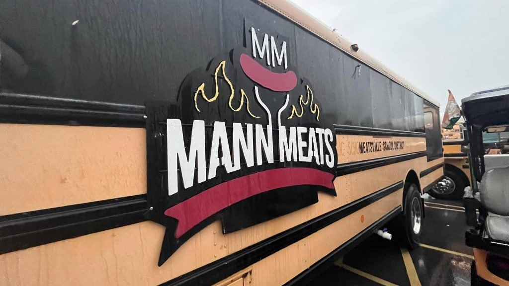 Mann Meats Florissant food truck parked in Missouri, featuring the original black and yellow school bus design with the Mann Meats BBQ logo.